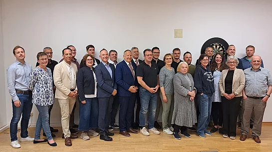 MGR 2026 - 2032 Gruppe von Menschen (neugewählter Marktgemeinderat) in einem Raum vor einer Dartscheibe an der Wand