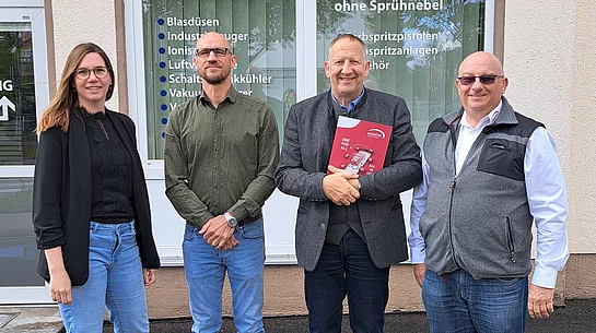 Vier Personen stehen vor einem Gebäude mit Schildern der Firma eputec Drucklufttechnik