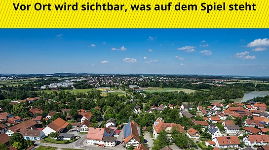 Luftaufnahme von Kaufering mit Wohnhäusern und viel Grün unter blauem Himmel, darüber gelber Balken mit dem Text 'GEMEINSAM EIN ZEICHEN SETZEN Vor Ort wird sichtbar, was auf dem Spiel steht' und darunter gelber Balken mit dem Text 'KOMMUNEN AM LIMIT'